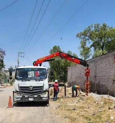 Camión grúa con trabajadores instalando poste en campo